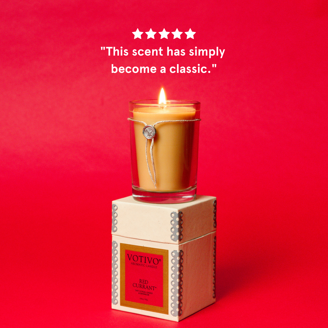A Votivo Red Currant 6.8 oz. Aromatic Candle burns atop its box against a red backdrop. Above, five stars and the quote: “This scent has simply become a classic” highlight the signature fragrance’s acclaim.