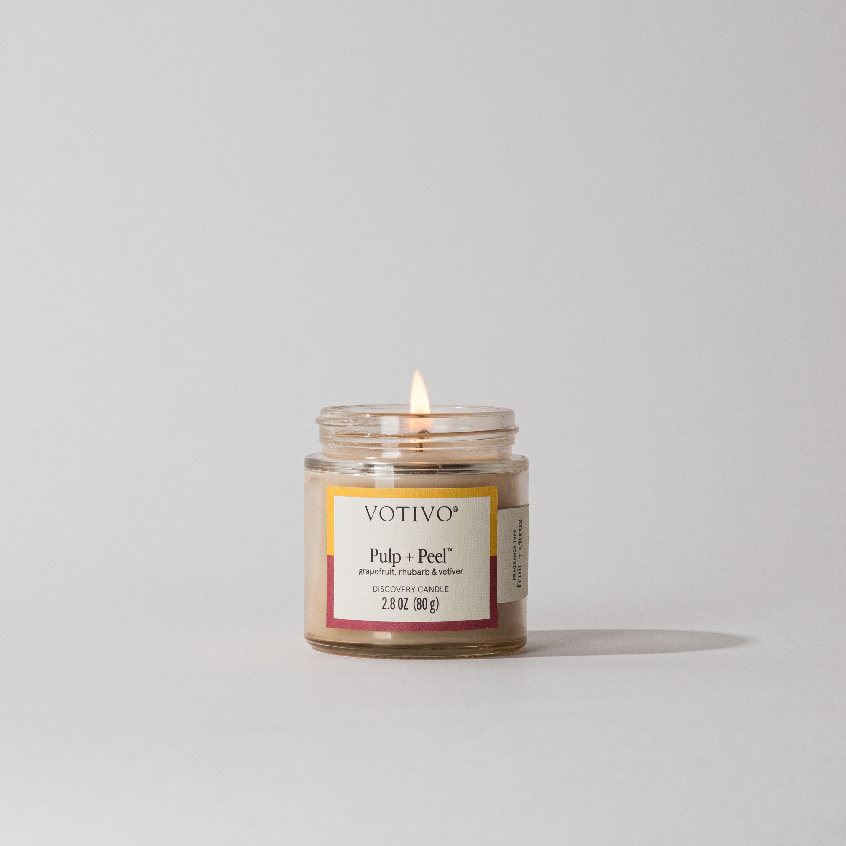 The Votivo Pulp + Peel Discovery Candle, displayed in a clear glass jar on a white surface, features premium soy blend wax for long-lasting fragrance.