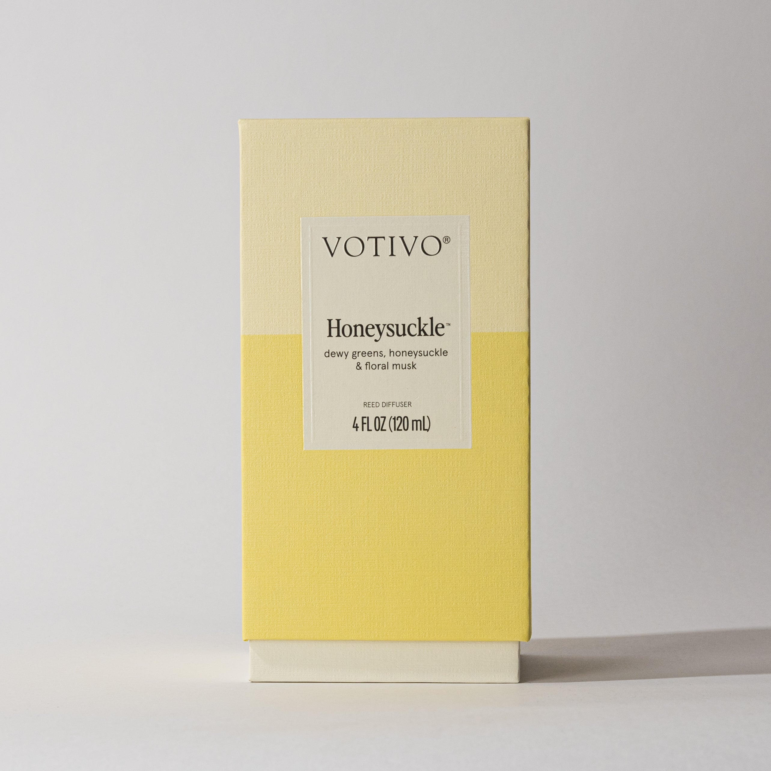 A rectangular cream and yellow Votivo Honeysuckle Reed Diffuser box features dewy greens, honeysuckle, and floral musk. Includes a 4 fl oz diffuser with fiber reeds, displayed on a light surface.