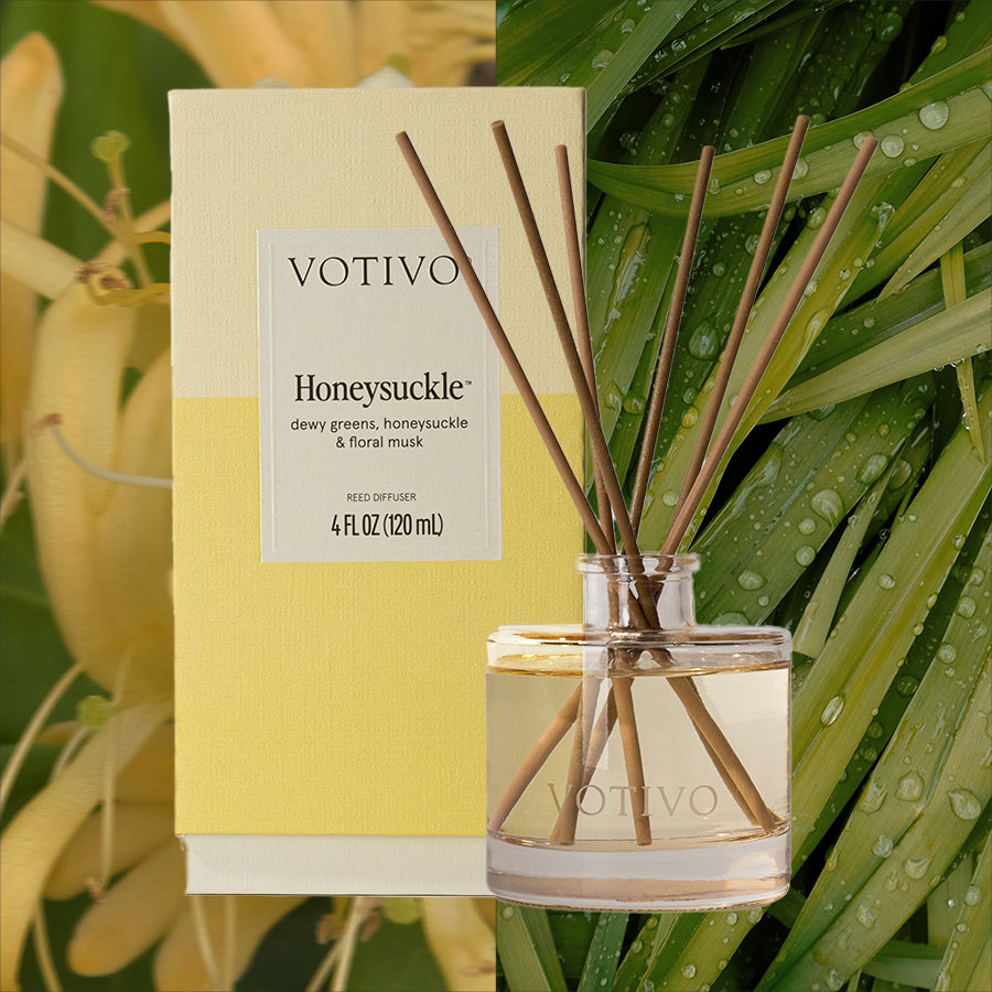 A Votivo Honeysuckle Reed Diffuser with fiber reeds and a yellow box stands before a split background of yellow honeysuckle flowers and fresh green leaves.