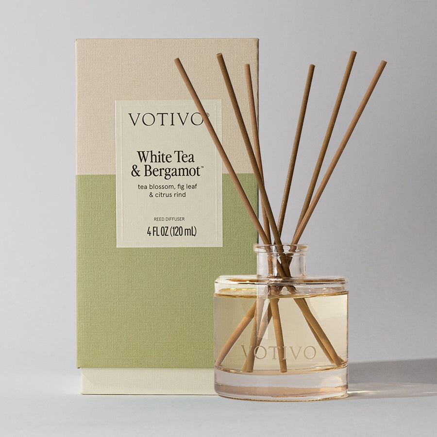 The Votivo White Tea + Bergamot Reed Diffuser, 4 fl oz (120 ml), with fiber reeds, stands in front of its box and features notes of tea blossom, fig leaf, and citrus rind.