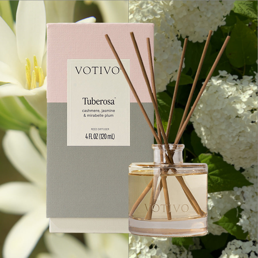 The Votivo Tuberosa Reed Diffuser and its box are shown. The box features the scent "Tuberosa: cashmere, jasmine & mirabelle plum." Fiber reeds and white flowers with green leaves are in the background.