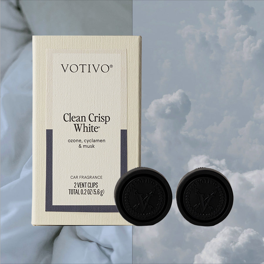 A Votivo Clean Crisp White Car Fragrance (2 Pack) is displayed with two black vent clips against a cloudy sky, showcasing its fresh scent blend of ozone, cyclamen, and musk.