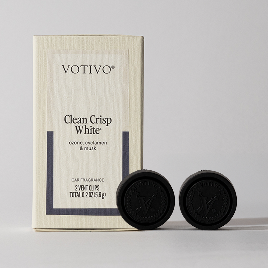 A Votivo Clean Crisp White Car Fragrance (2 Pack) stands upright next to two black vent clips with embossed Votivo logos, adding a fresh scent to any vehicle, all displayed against a neutral background.