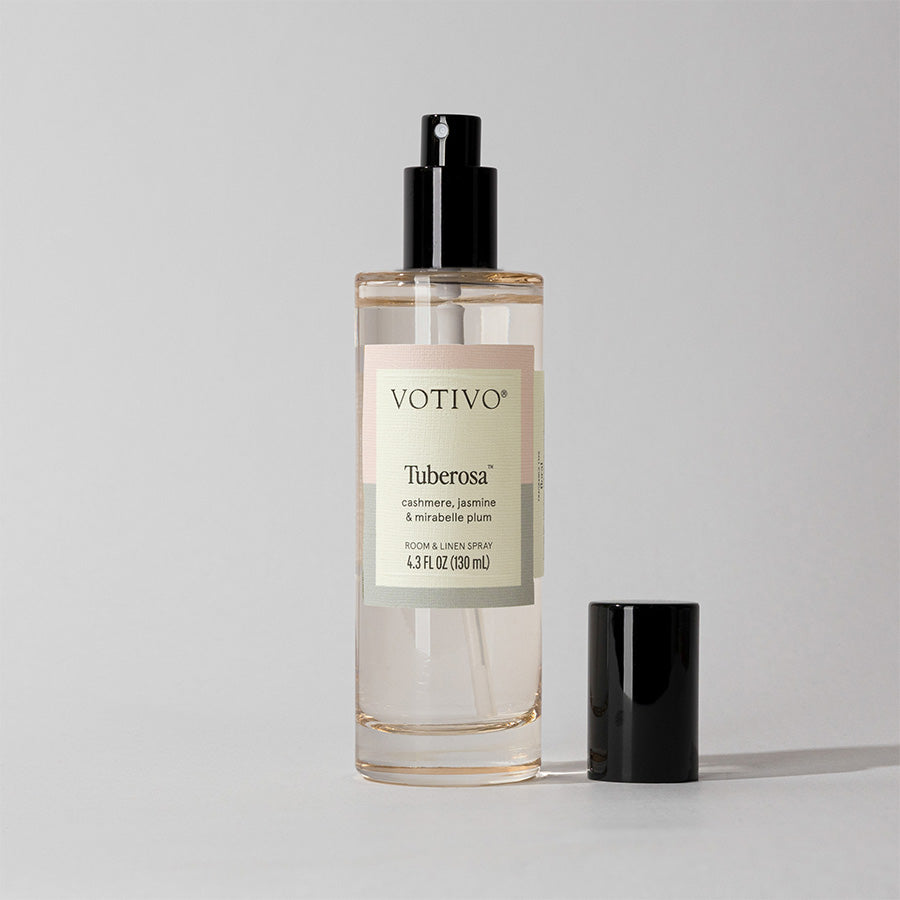 A clear Votivo Tuberosa Room & Linen Spray bottle with a black nozzle and cap, set on a light gray background, delivers a luxurious tuberose scent that’s safe for use as both a room and fabric spray.