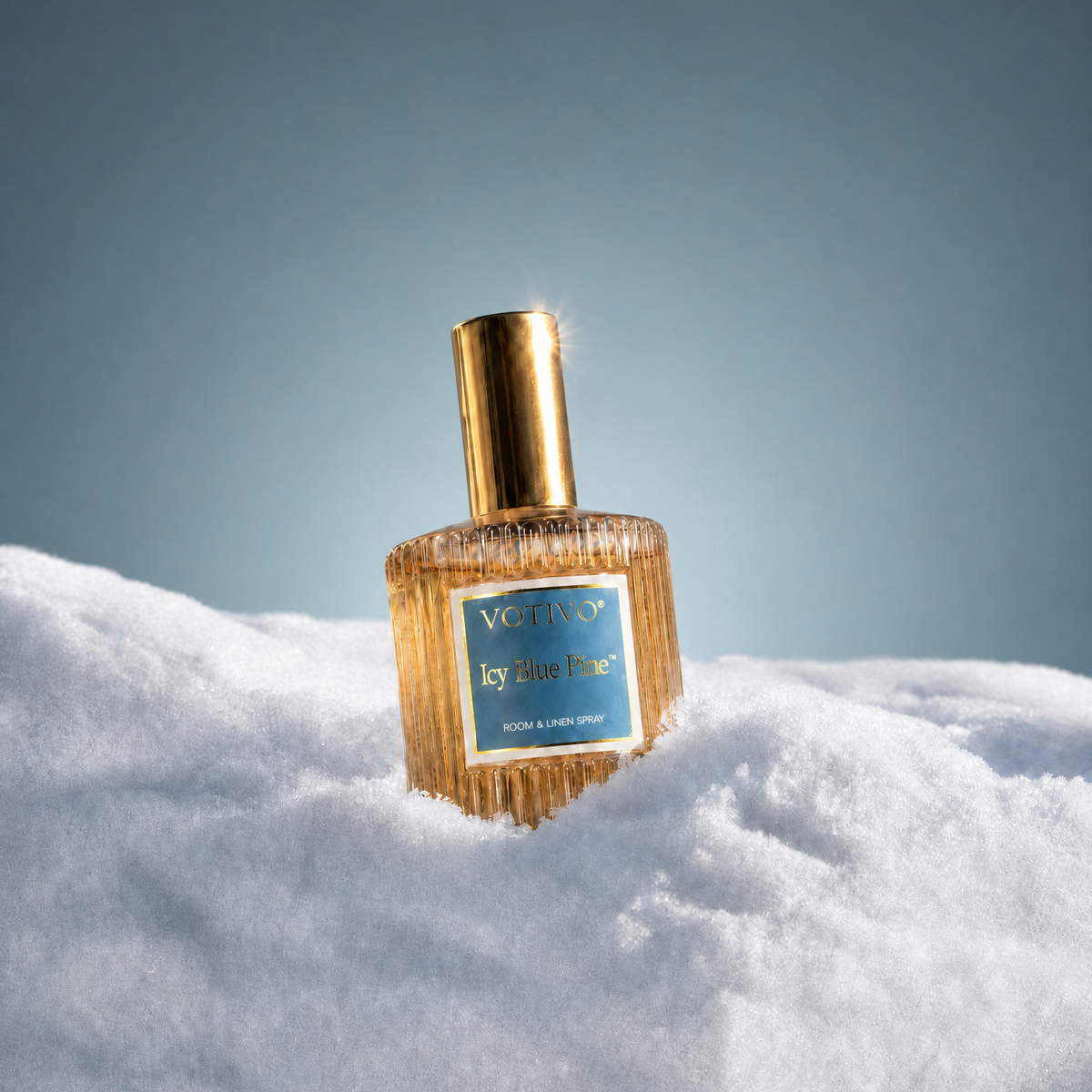 A Votivo Icy Blue Pine room & linen spray bottle sitting in a pile of white fluffy snow
