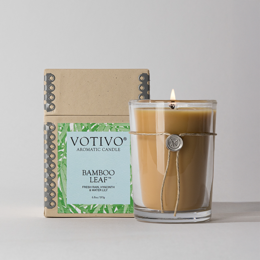 The Votivo Bamboo Leaf 6.8 oz. Aromatic Candle, made from a soy blend for a clean, lasting fragrance, features a glass jar with string and coin accents and comes in cardboard box packaging.