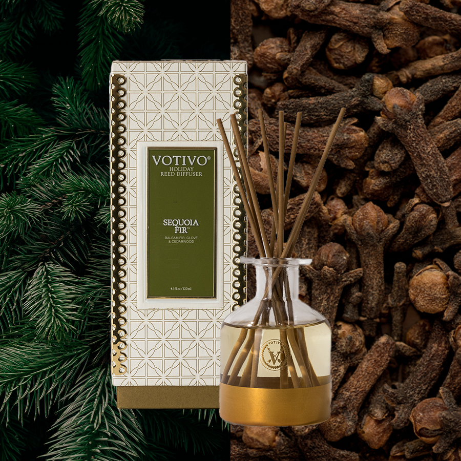 The Votivo Sequoia Fir Holiday Reed Diffuser and its box sit between pine needles and dried cloves, with rattan reeds adding to the festive, aromatic vibe.