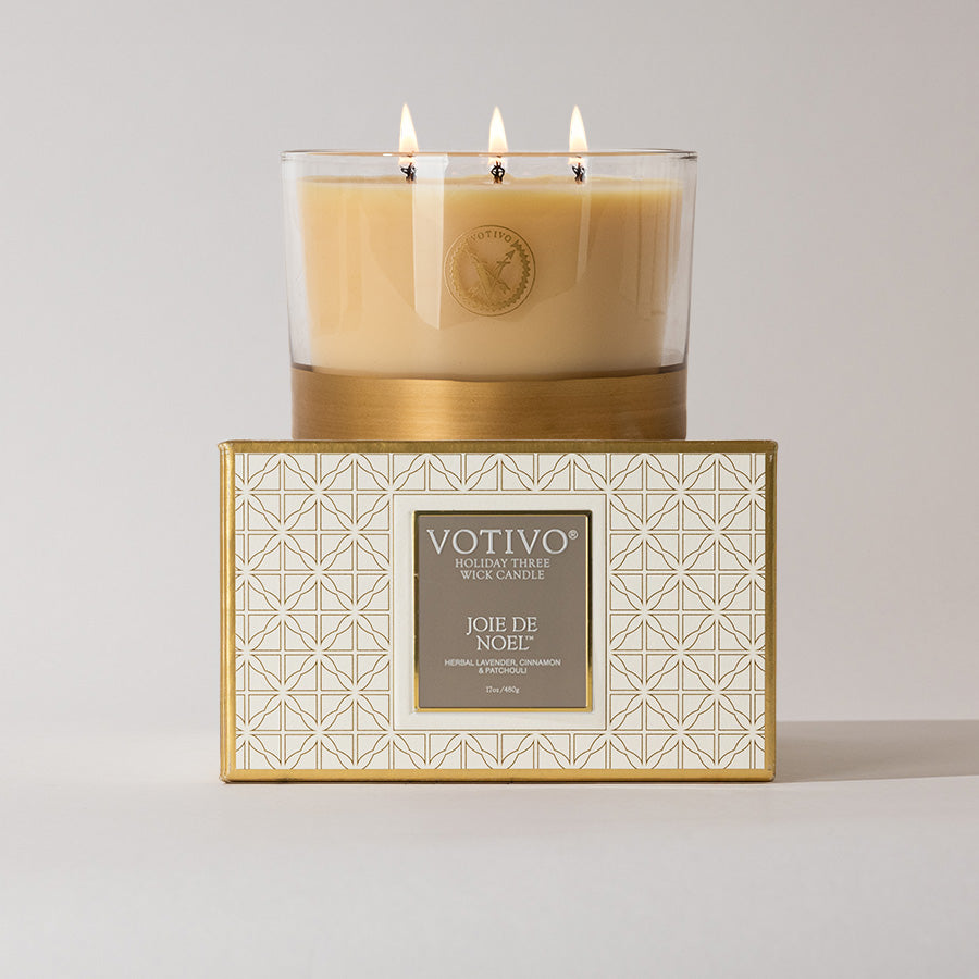 The Votivo Joie de Noel Holiday 3 Wick Candle sits on its gold and white geometric box, filling your home with festive fragrance. This luxurious soy blend candle’s three glowing wicks create a radiant holiday ambiance.