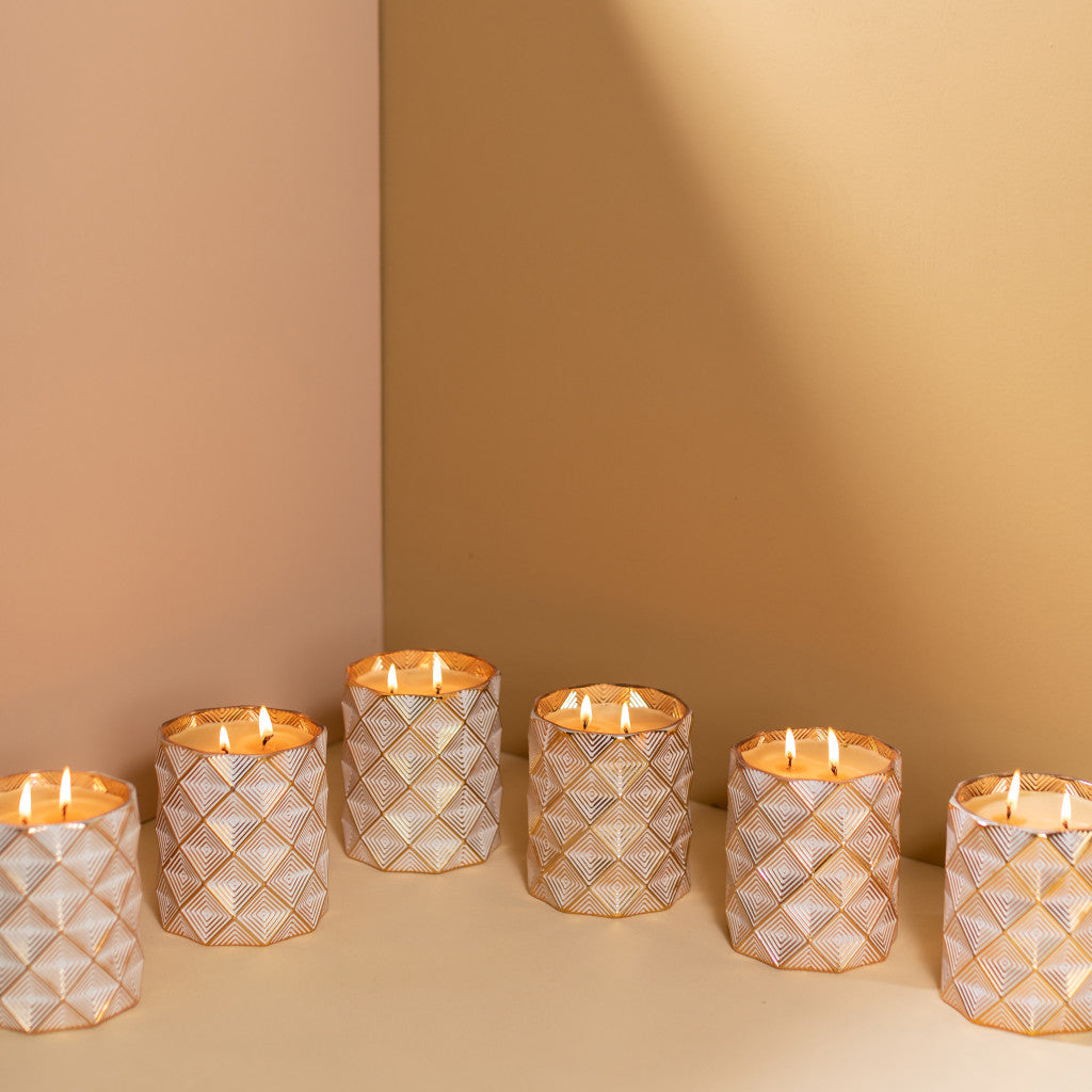 Six Votivo Icy Blue Pine Holiday Decorative Candles in textured white and gold holders are arranged on a beige surface, casting soft shadows—each a stylish soy blend candle, ideal for adding warmth to any space.