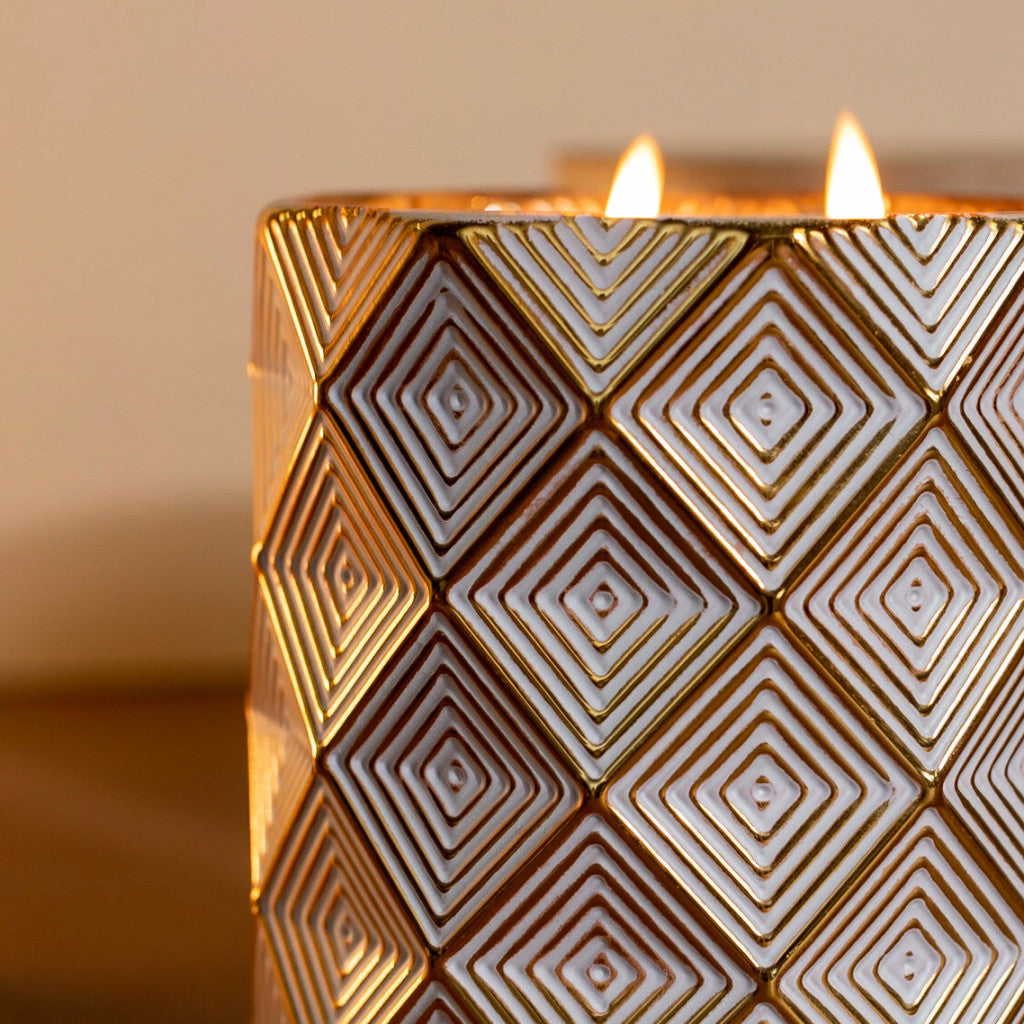A close-up of Votivo’s Icy Blue Pine Holiday Decorative Candle, a soy blend candle in a geometric gold and white holder. Two flames glow warmly, making it the perfect decorative piece for cozy spaces.