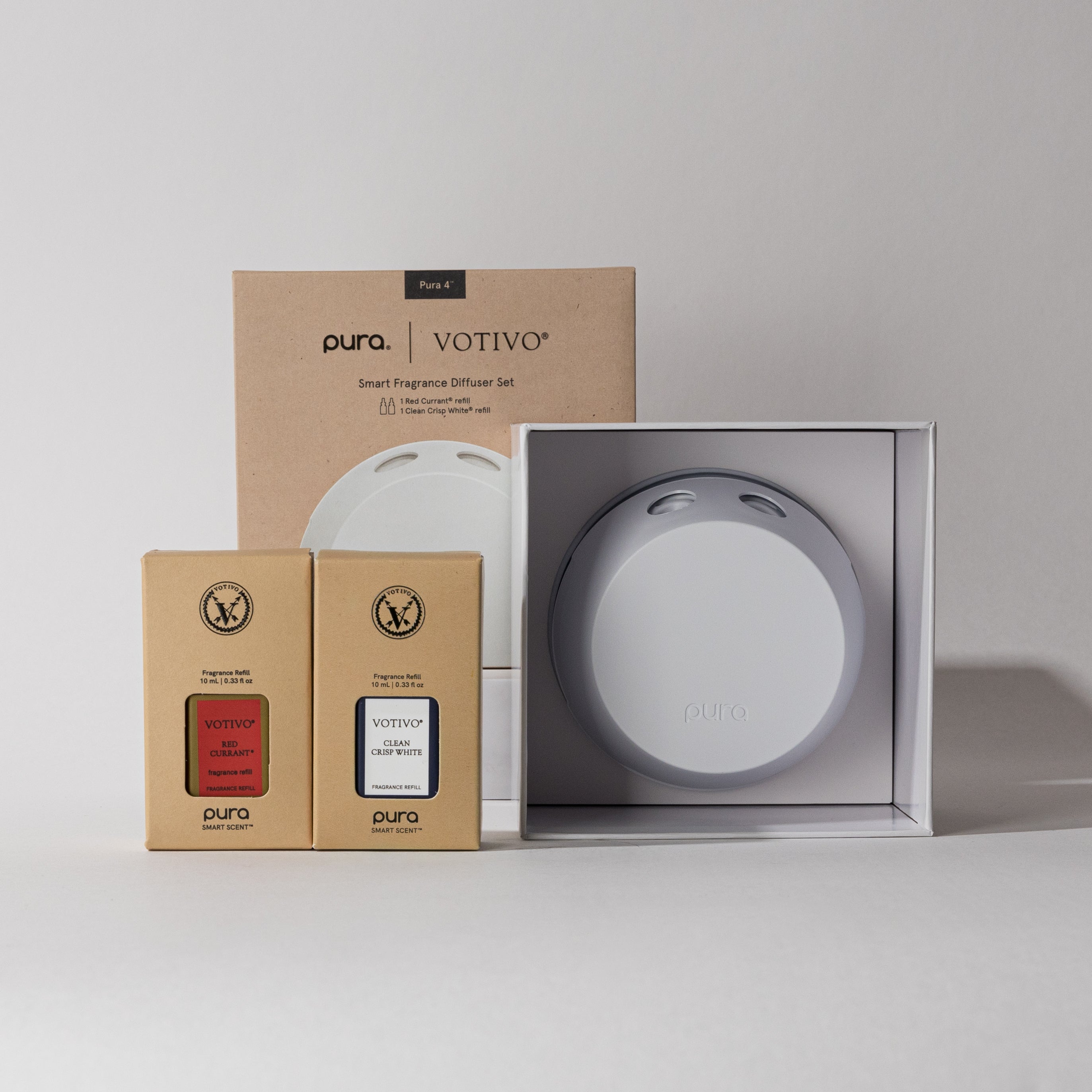 The Votivo Red Currant & Clean Crisp White Pura + Votivo Smart Home Diffuser Set is shown with the diffuser in an open white box and two fragrance refills, offering customizable scent intensity.