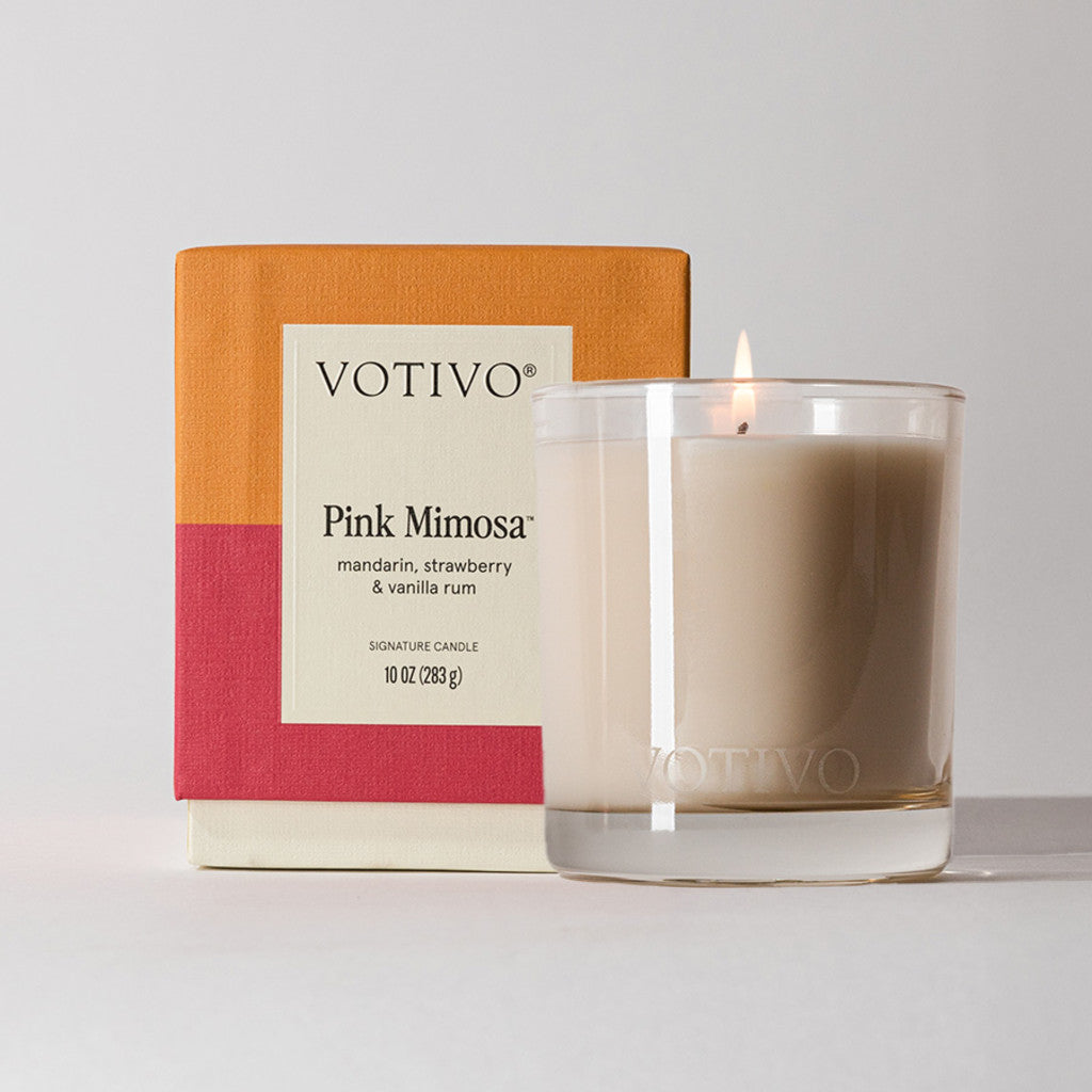 The Votivo Pink Mimosa 10 oz. Signature Candle fills your space with mandarin, strawberry, and vanilla rum aromas. Its clear glass jar showcases a soy blend wax and comes in a vibrant orange, red, and cream box.