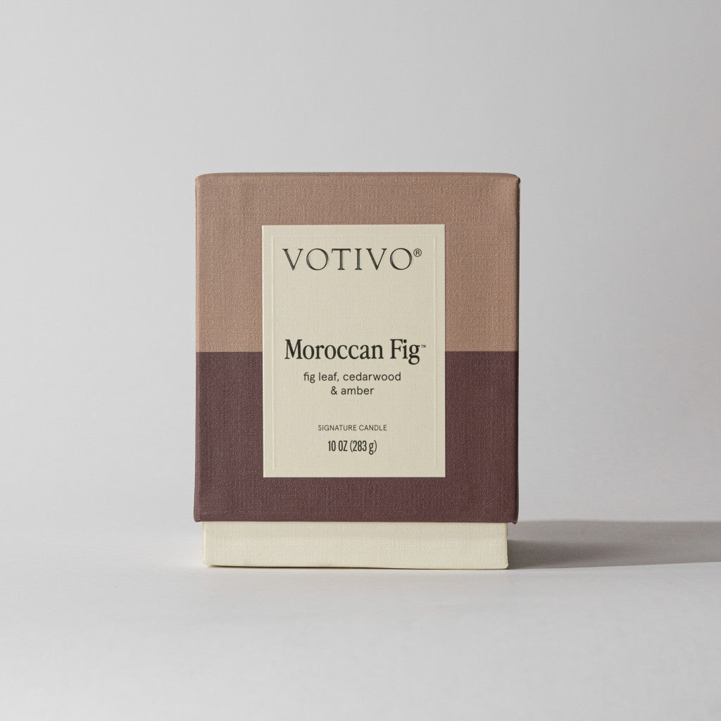 A Votivo Moroccan Fig 10 oz. Signature Candle in a minimalist beige, taupe, and brown box features notes of fig leaf, cedarwood, and amber. Made with soy blend wax, the candle is shown against a plain background.
