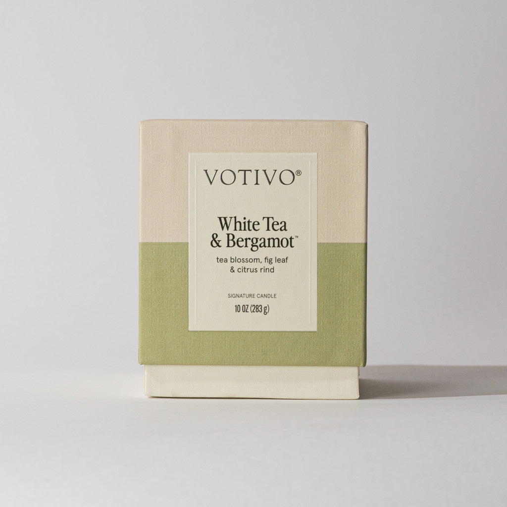 The Votivo White Tea & Bergamot 10 oz. Signature Candle features a soy blend wax, elegant cream and green design, and a scent of tea blossom, fig leaf, and citrus rind.