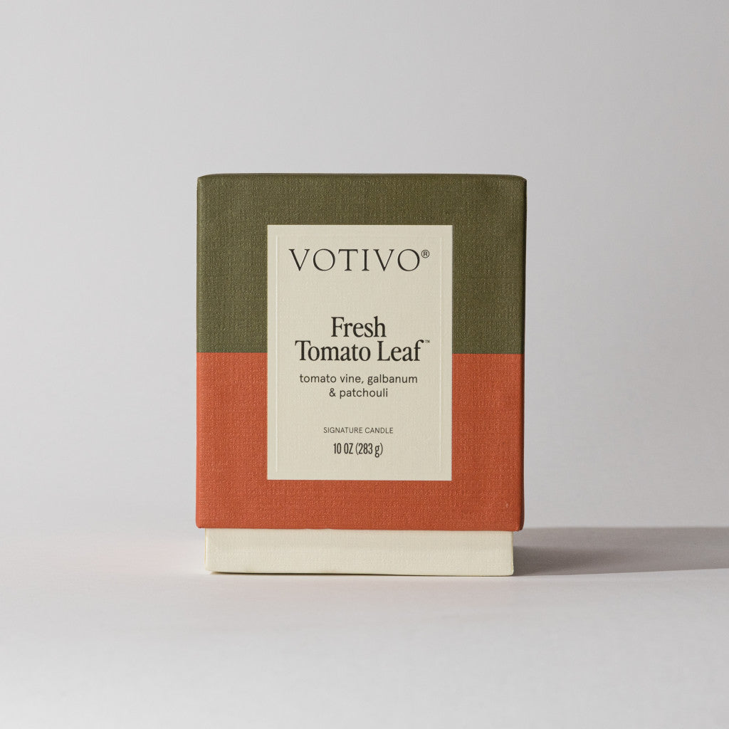 The Votivo Fresh Tomato Leaf 10 oz. Signature Candle features scent notes of tomato vine, galbanum, and patchouli in a soy blend wax, boxed in olive green, rust orange, and cream color blocks.