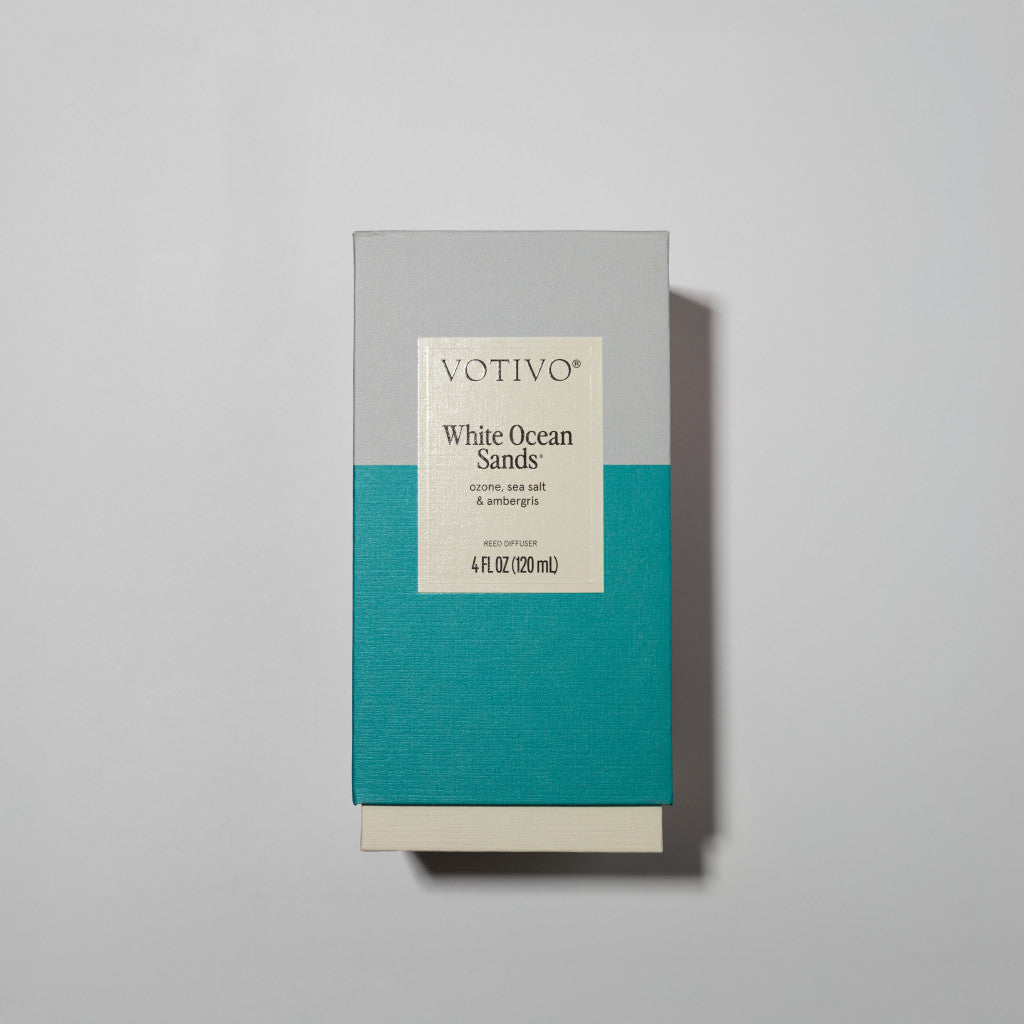 A rectangular Votivo box in gray and teal labeled White Ocean Sands hints at the White Ocean Sands Reed Diffuser inside, photographed against a plain light gray background.