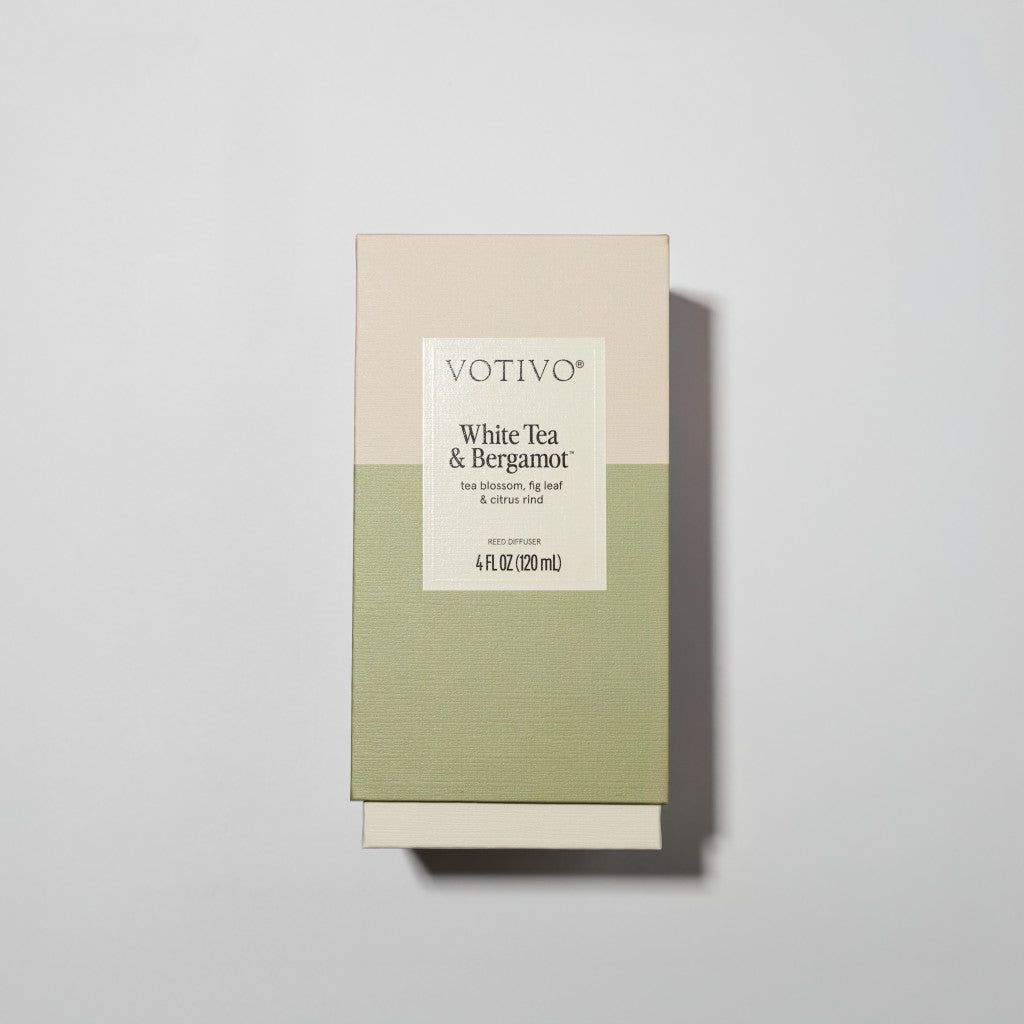 A rectangular Votivo White Tea + Bergamot Reed Diffuser box features fiber reeds, a minimalist beige and light green design, and 4 fl oz of fragrance with notes of tea, blossoms, fig, and citrus.