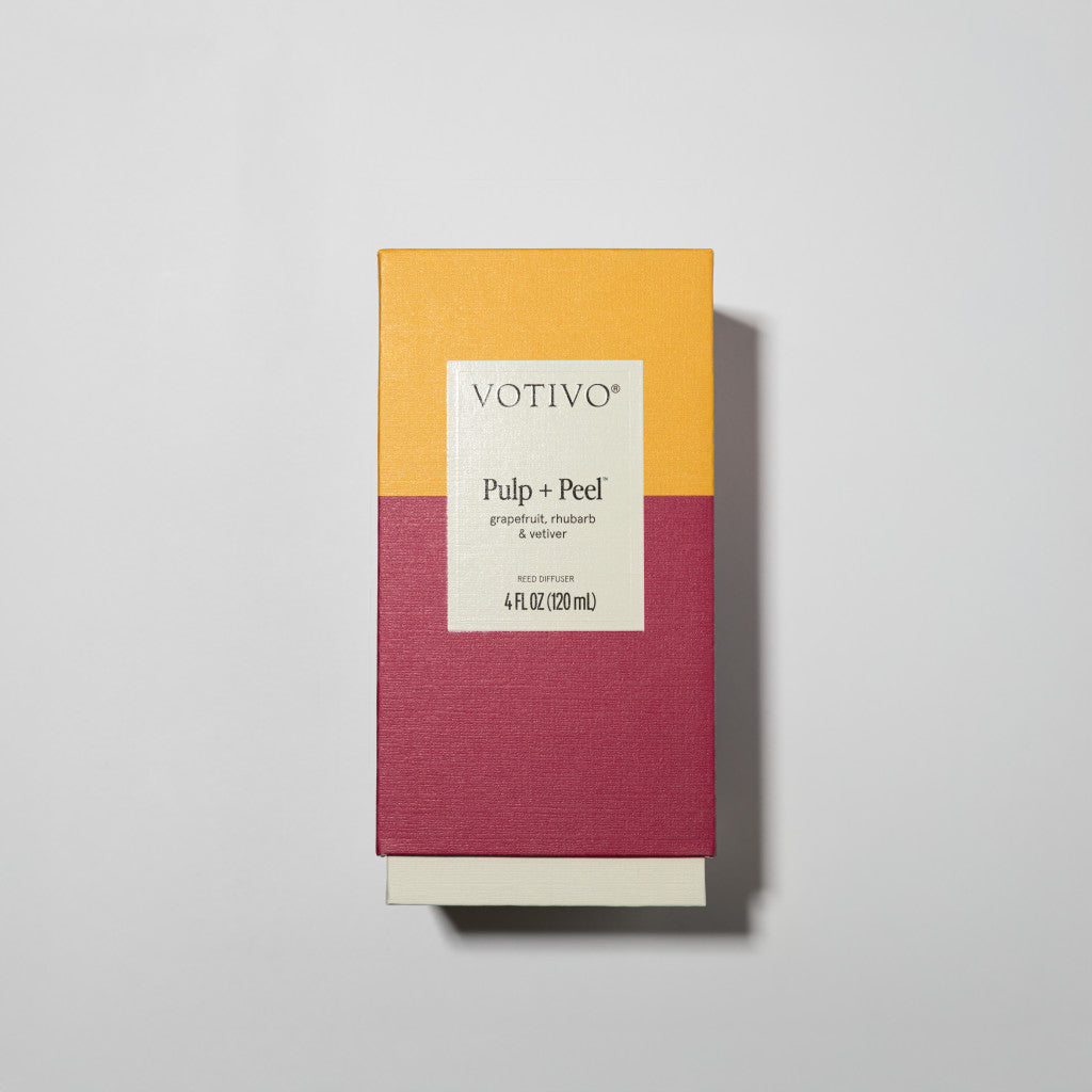 A Votivo Pulp + Peel Reed Diffuser box with grapefruit and rhubarb scent features a yellow top, maroon bottom, and white label. It sits on a light background, ideal for pairing with the matching candle for lasting fragrance.