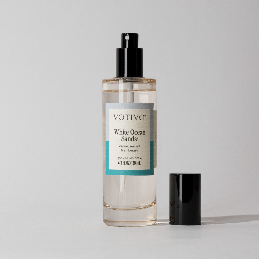 The Votivo White Ocean Sands Room & Linen Spray, in a clear bottle with a black nozzle and cap, sits against a light background, offering a refreshing fragrance to your space.
