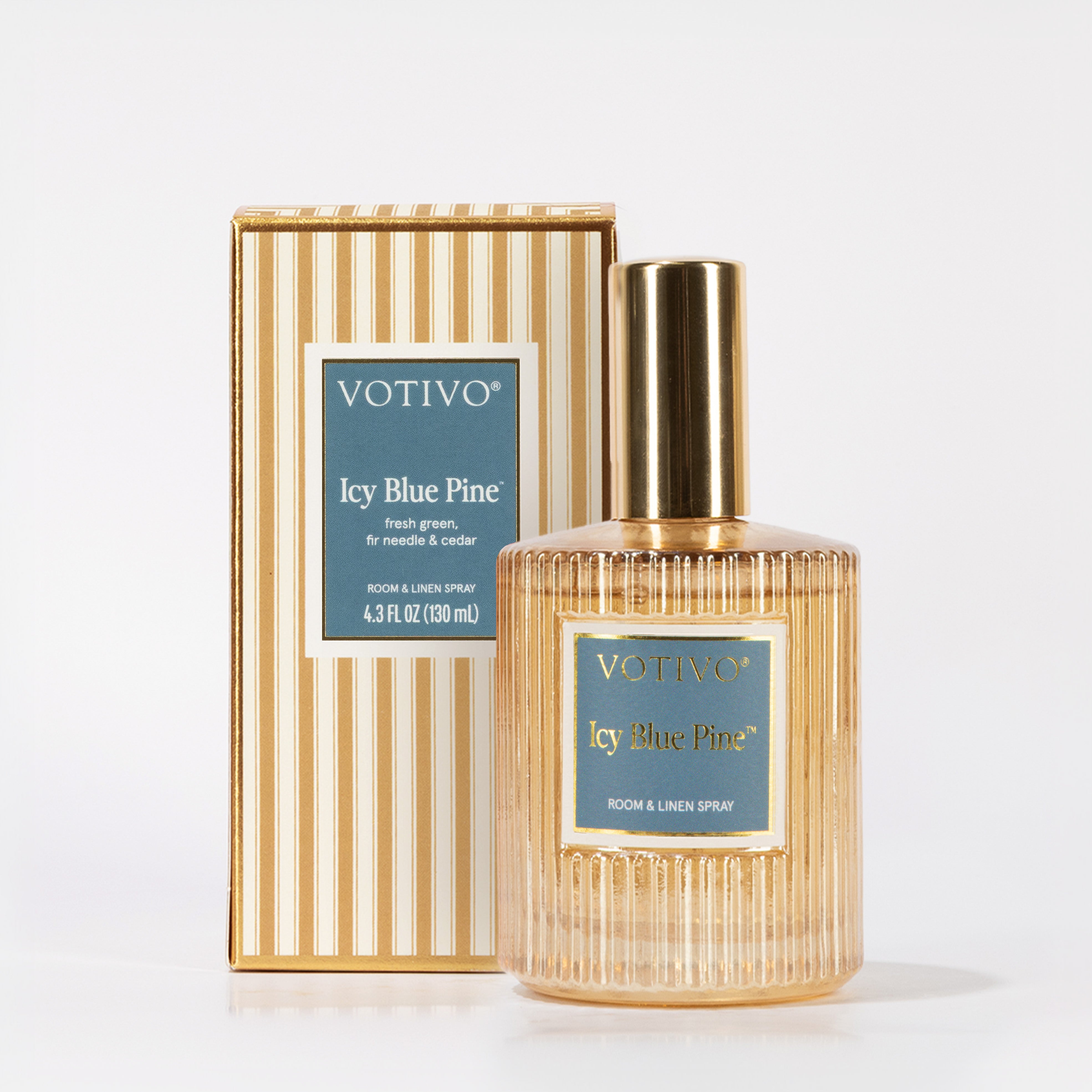 A bottle of Votivo Icy Blue Pine Room & Linen Spray is displayed before its striped box, both showcasing blue labels with gold text. The bottle’s gold cap and ribbed glass add sophistication to this fresh home fragrance.