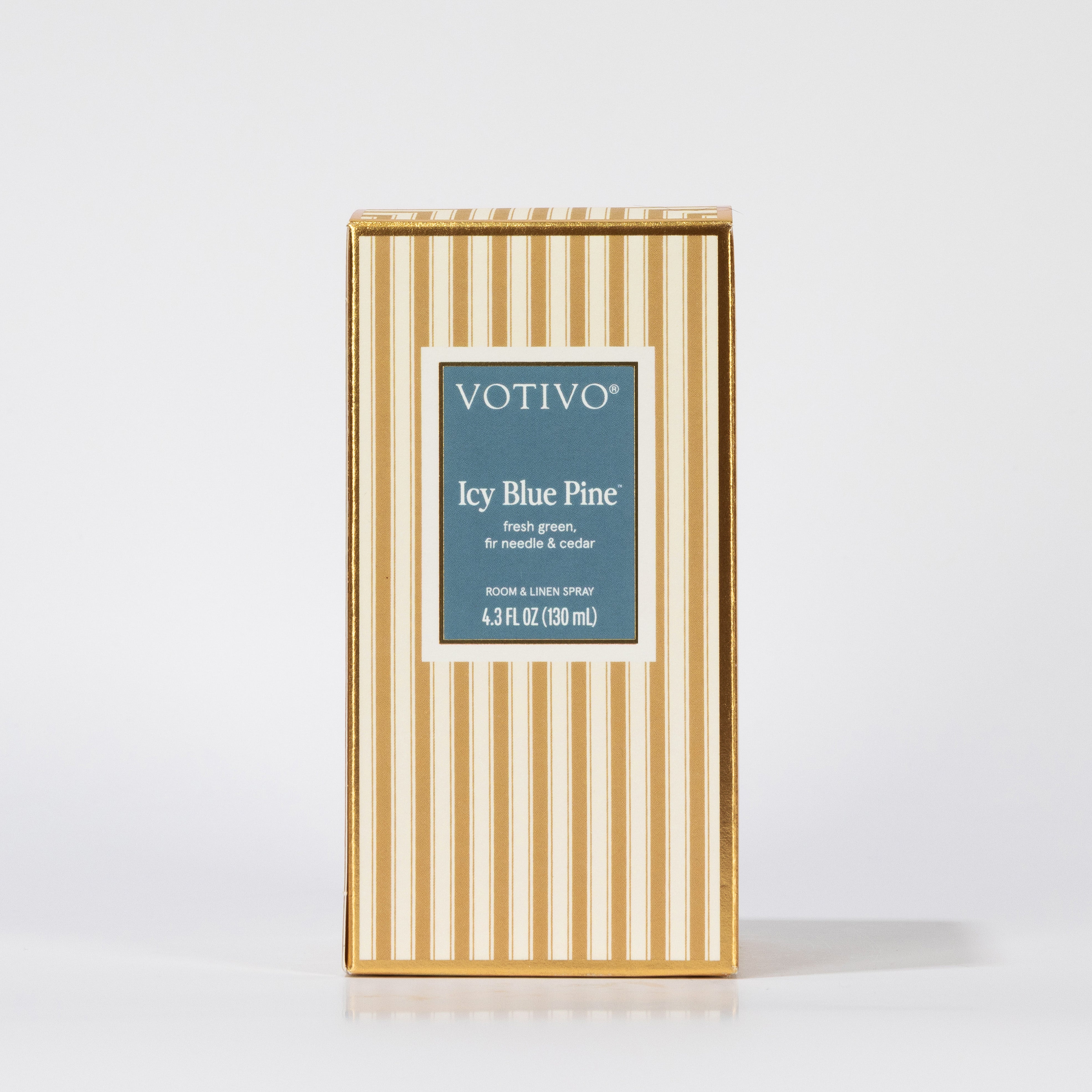 The Votivo Icy Blue Pine Room & Linen Spray features festive fresh green needles and cedar fragrance in a 4.3 FL OZ (130 mL) size, packaged in a rectangular box with vertical gold and white stripes.