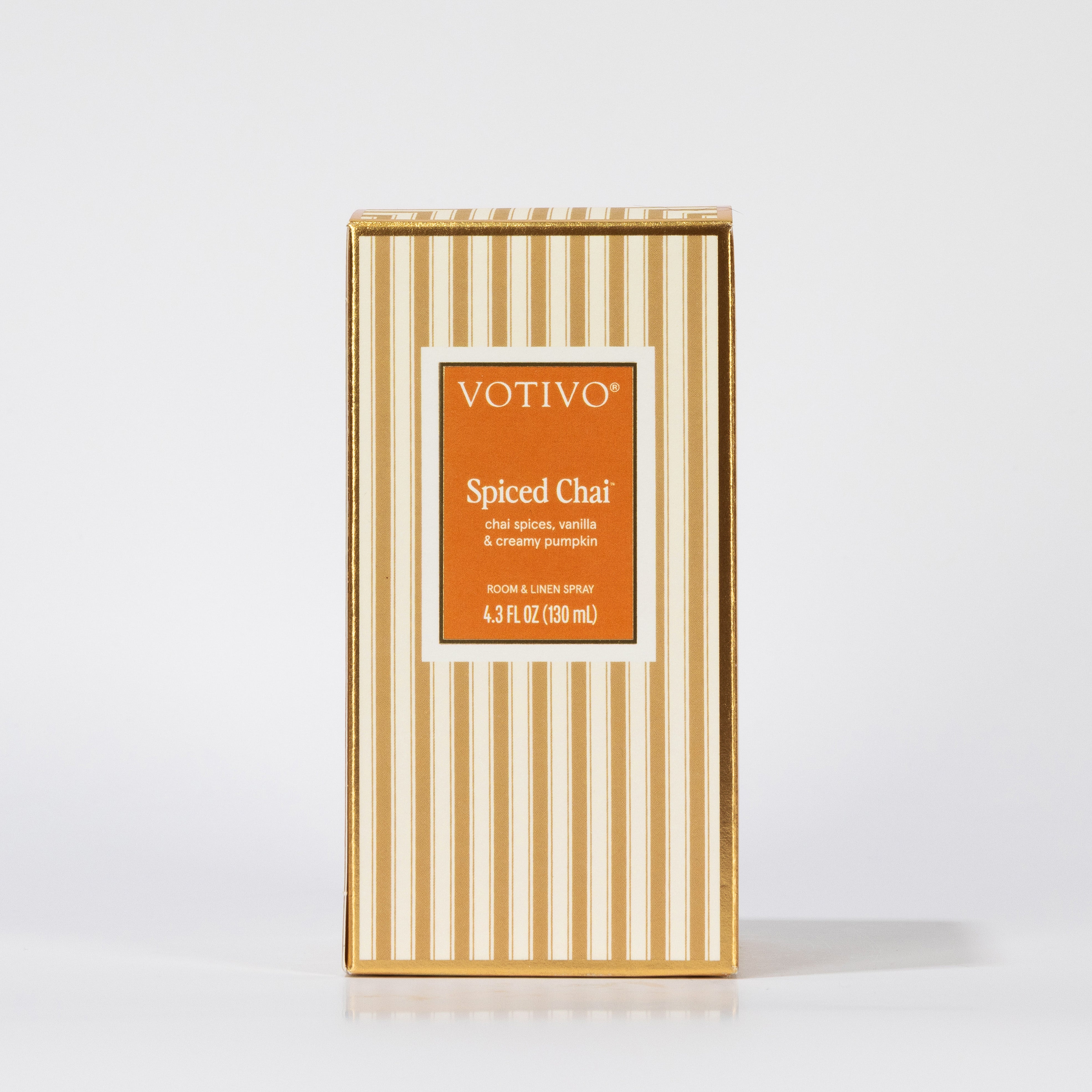 A rectangular box of Votivo Spiced Chai Room & Linen Spray features beige and white vertical stripes with an orange front label displaying the fabric-safe product name and scent details.