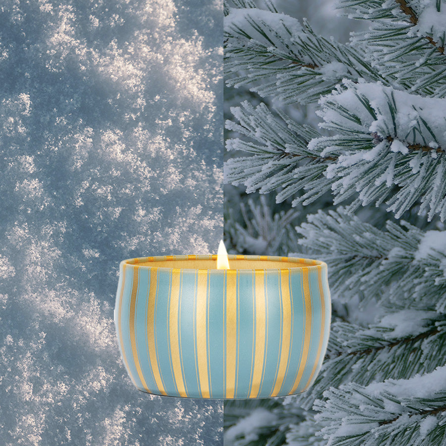 A glowing Votivo Icy Blue Pine Holiday Tin Candle sits centered in an image divided between snowy close-up and frosted pine branches, evoking a cozy winter scene.