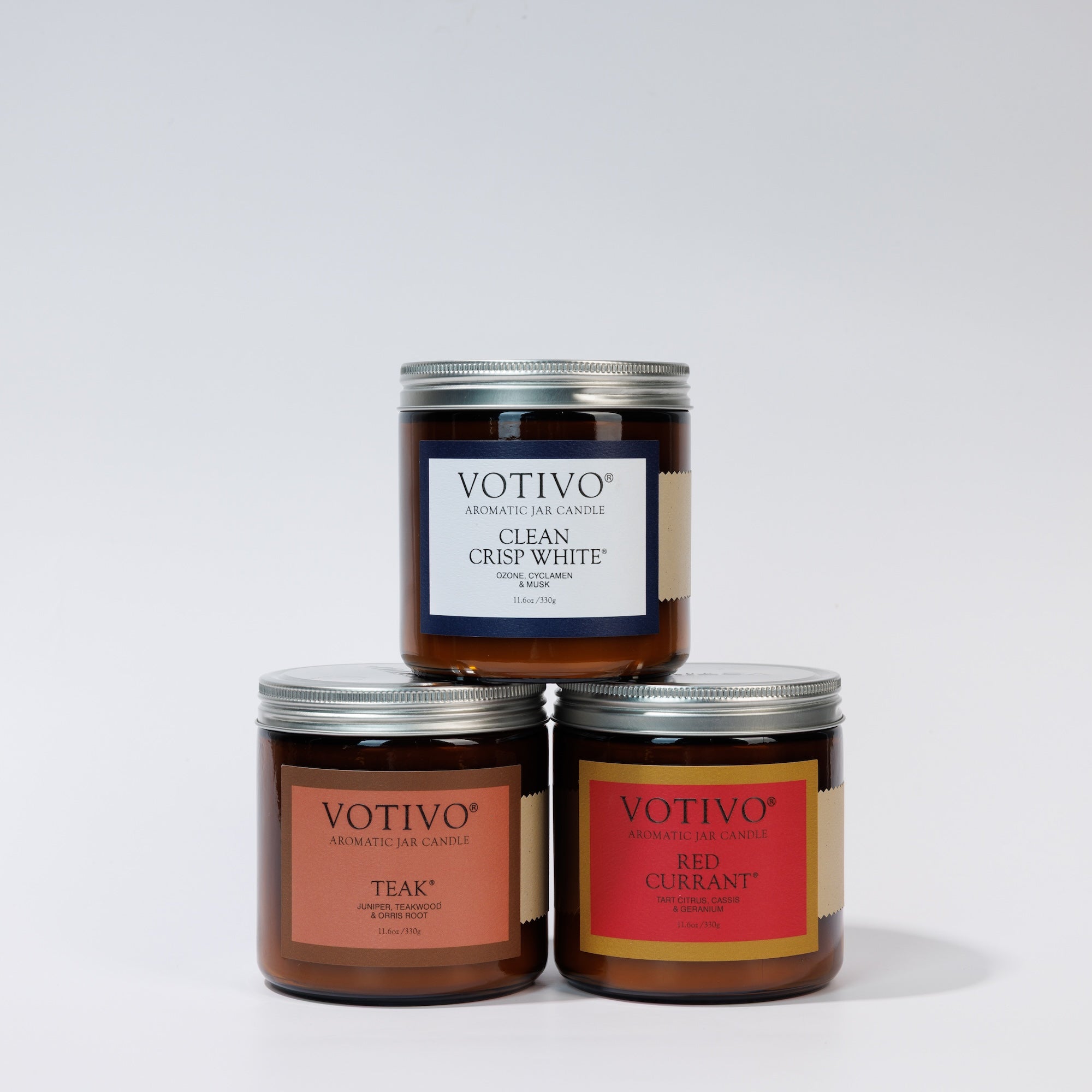Three large amber jar Votivo candles—Red Currant, Clean Crisp White & Teak—are stacked in this Limited Edition Candle Set, each with a chic metal lid and distinct white, red, or tan label for a stylish display.