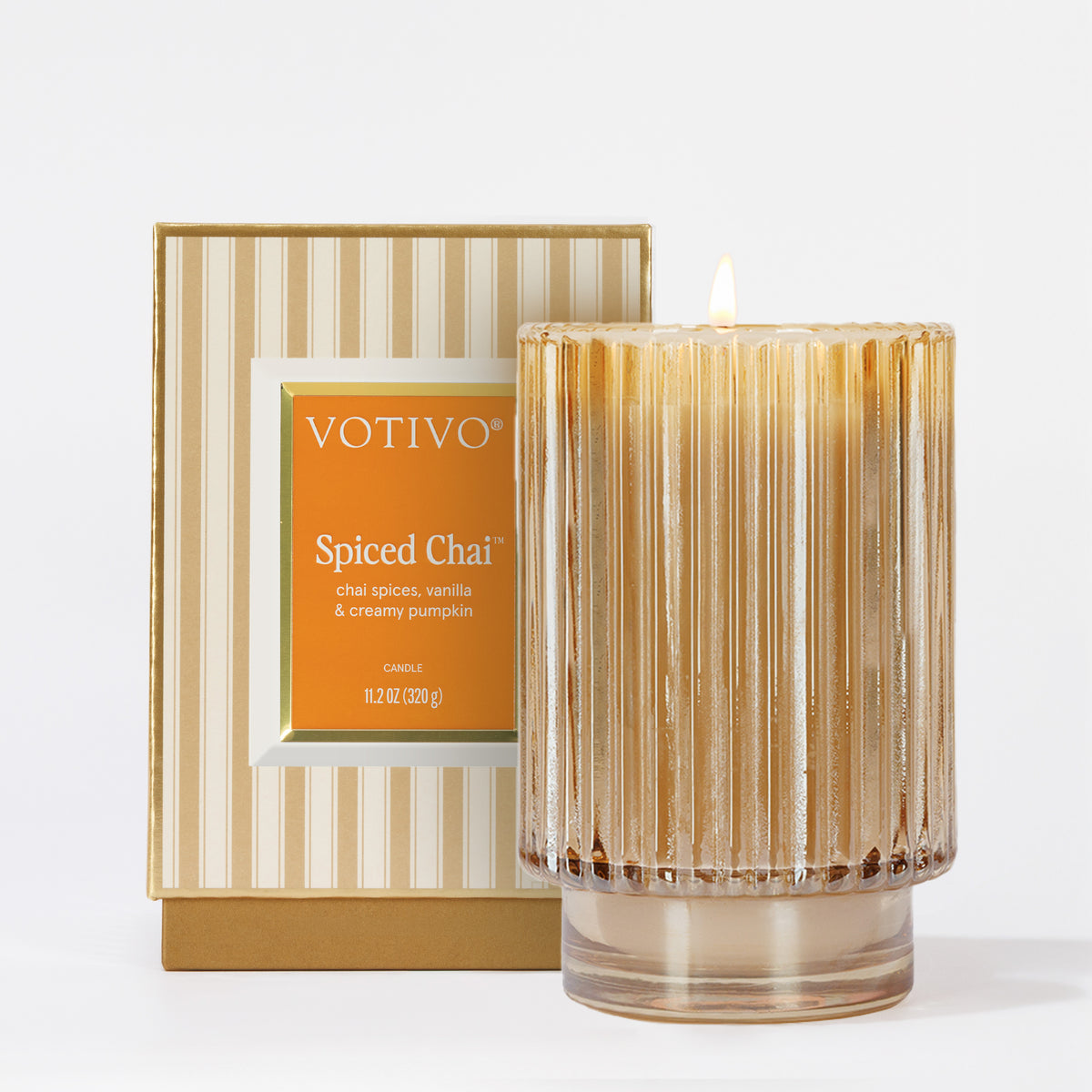 The Votivo Spiced Chai Holiday Candle features chai spices, vanilla, and creamy pumpkin in a soy blend wax. Its ribbed glass jar and gold-striped box add a cozy seasonal glow to any room.