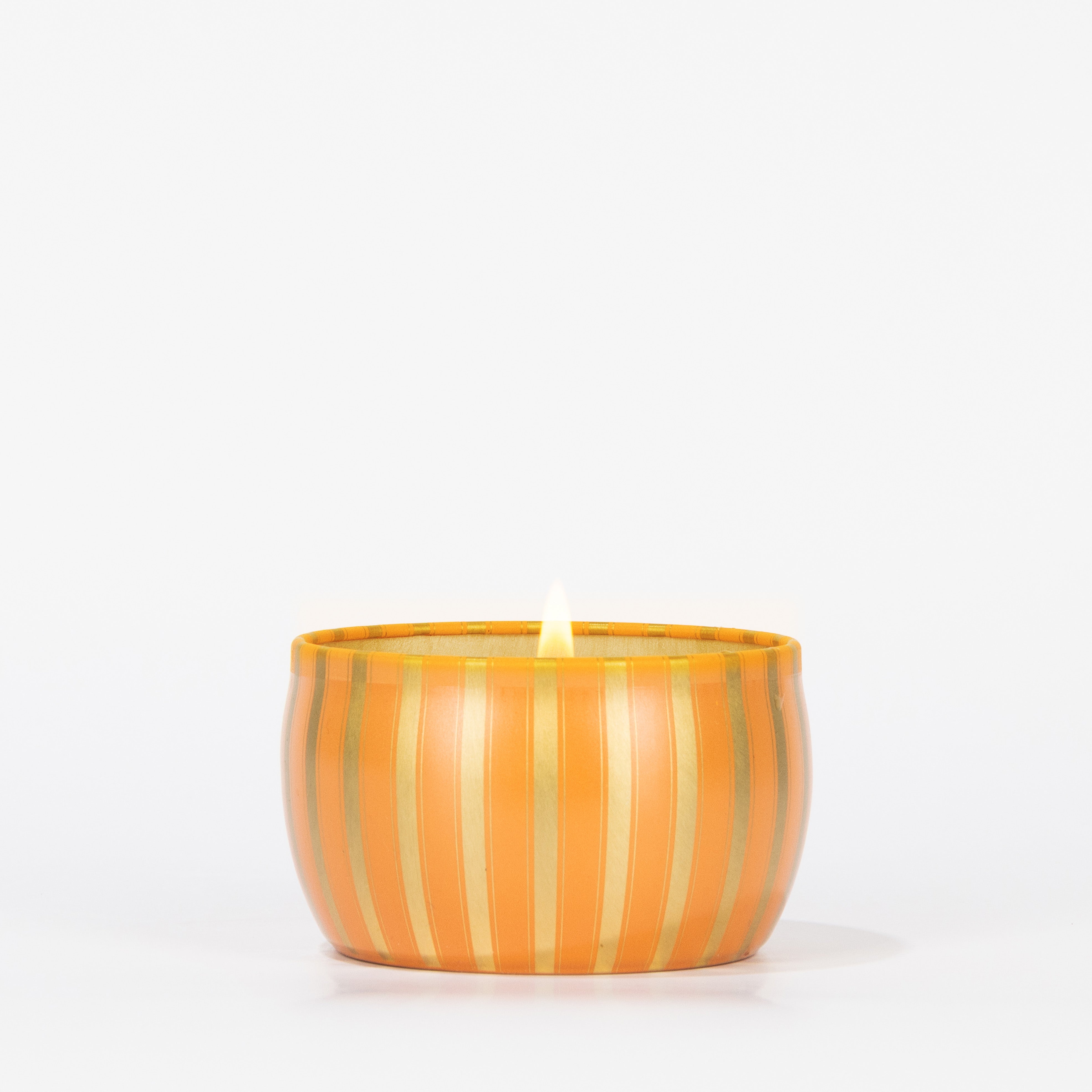 The Votivo Spiced Chai Holiday Tin Candle is a small soy blend candle in an orange and gold striped tin, filling your space with a warm spiced chai aroma.
