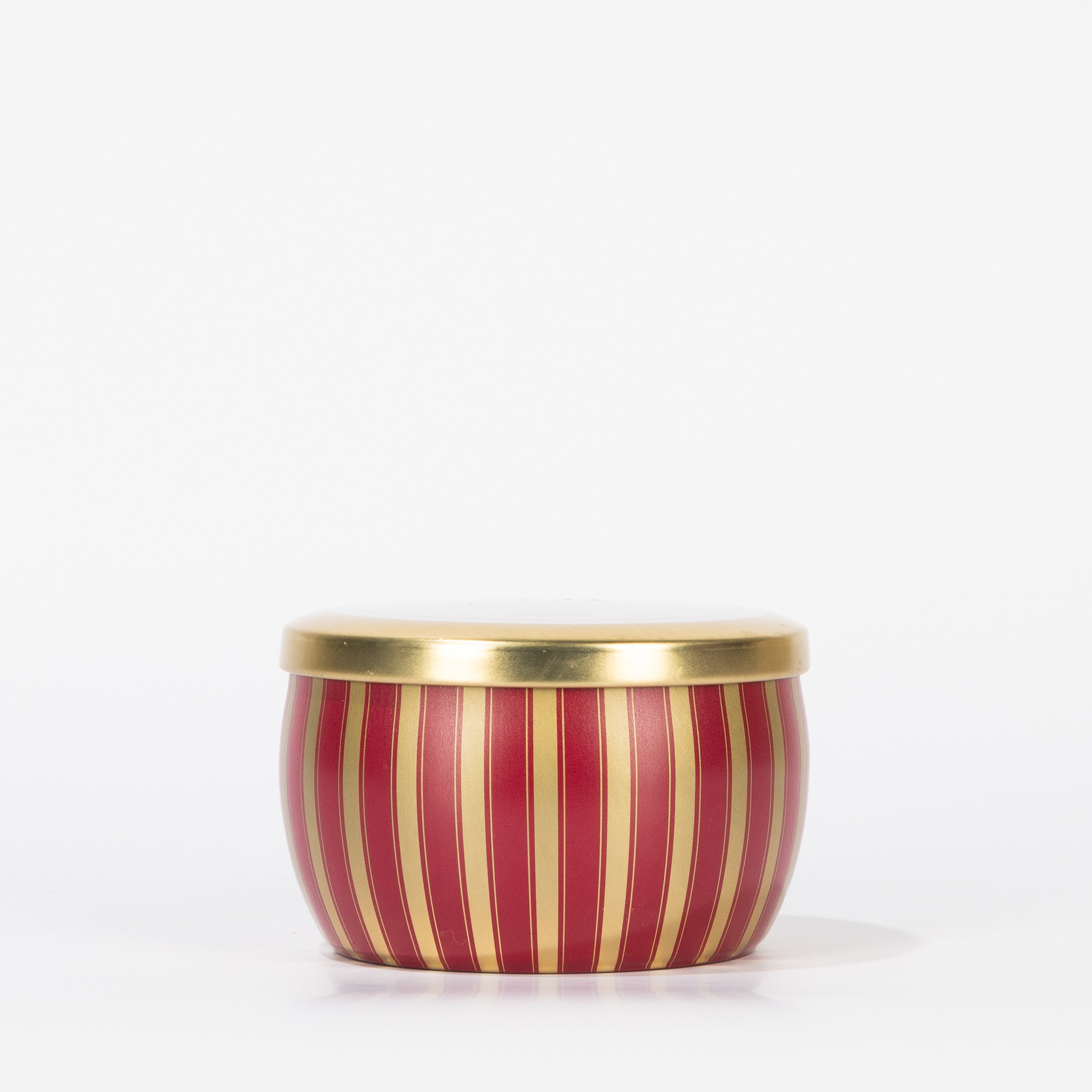 The Votivo Velvet Rouge Holiday Tin Candle features vertical red and gold stripes and a gold lid, displayed on a plain white background.