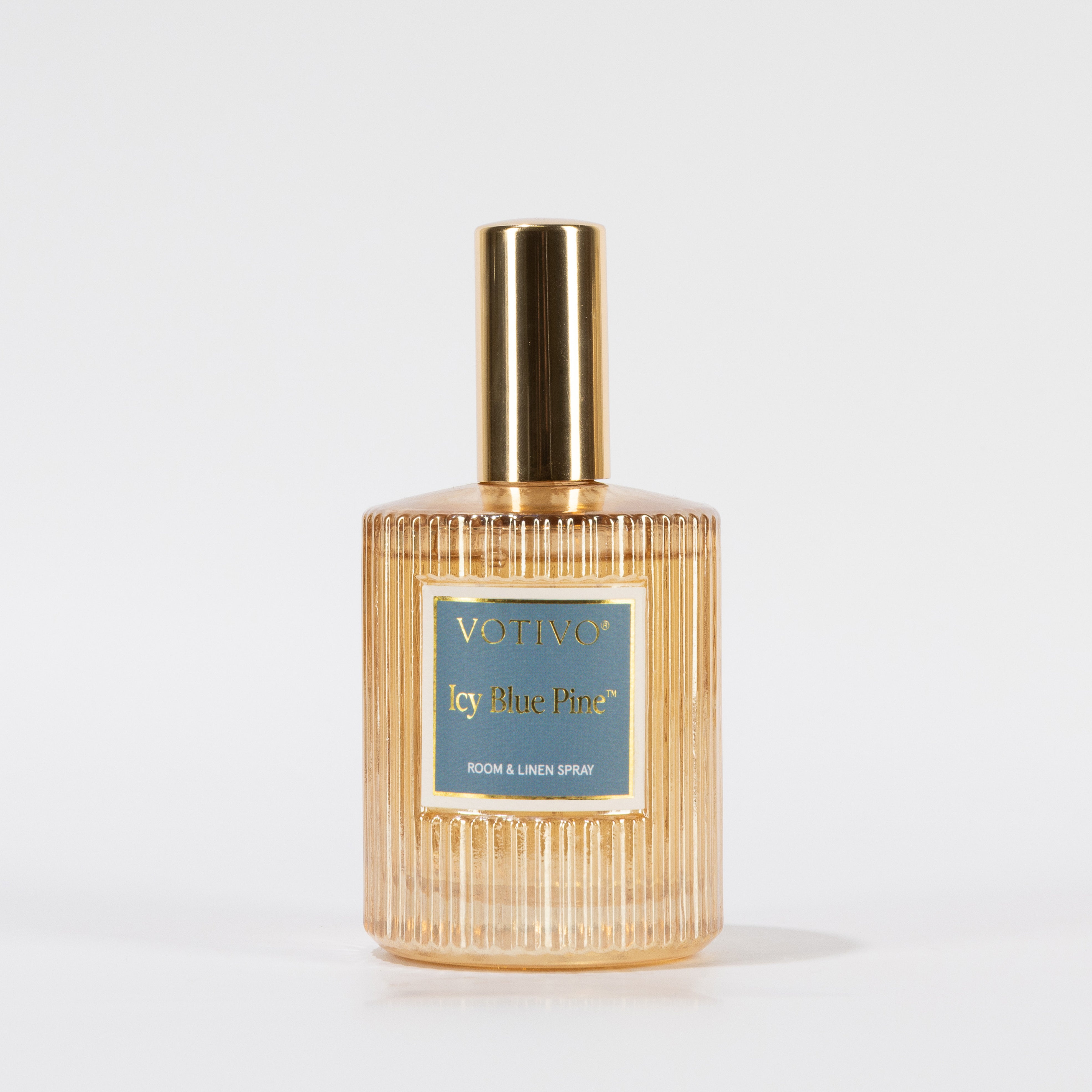 A gold and clear ribbed glass spray bottle labeled Votivo Icy Blue Pine Room & Linen Spray stands upright on a plain white background, ready to infuse your space with a fresh scent.