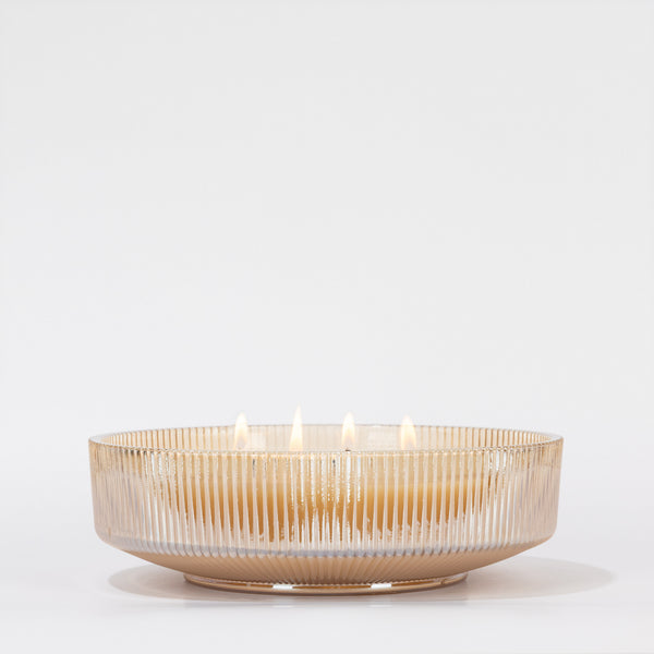 The Votivo Gilded Pear Holiday Multi-Wick Candle, set in a beige ribbed glass bowl with soy blend wax and multiple lit wicks, casts a warm holiday glow against a plain white background.
