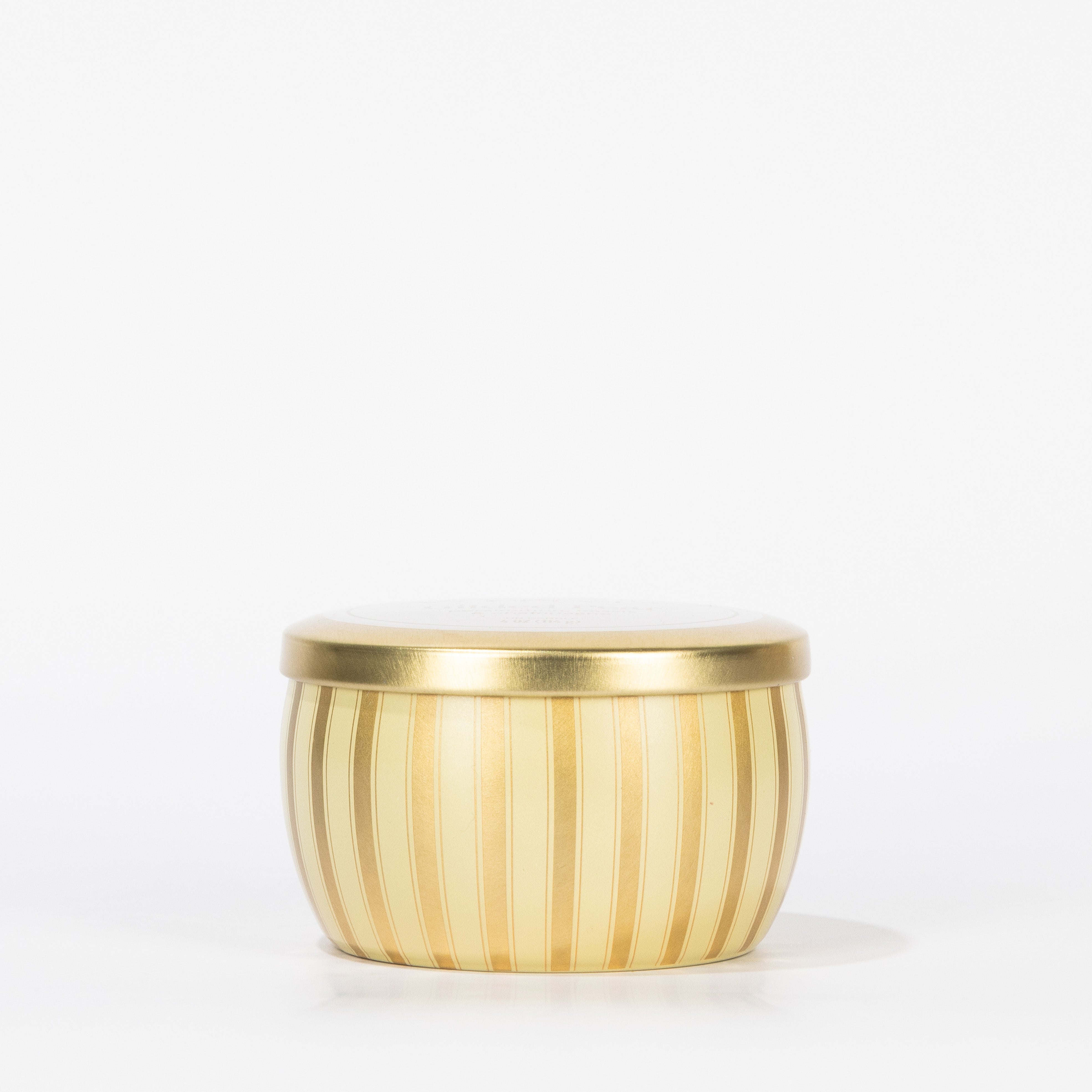 The Votivo Gilded Pear Holiday Tin Candle is a small, round, gold-colored tin with vertical stripes and a matching lid, filled with soy blend wax in a fragrant Gilded Pear scent, displayed against a plain white background.