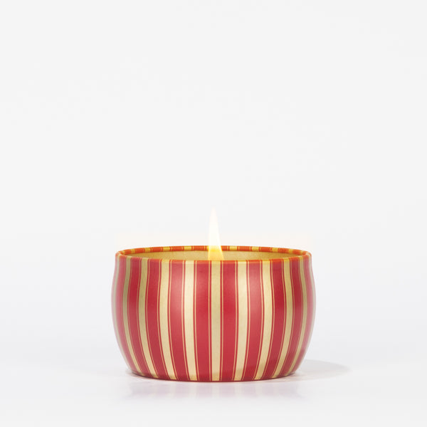 The Votivo Red Currant Holiday Tin Candle features a soy blend wax in a small, round tin with vertical red and gold stripes, displayed against a plain white background.