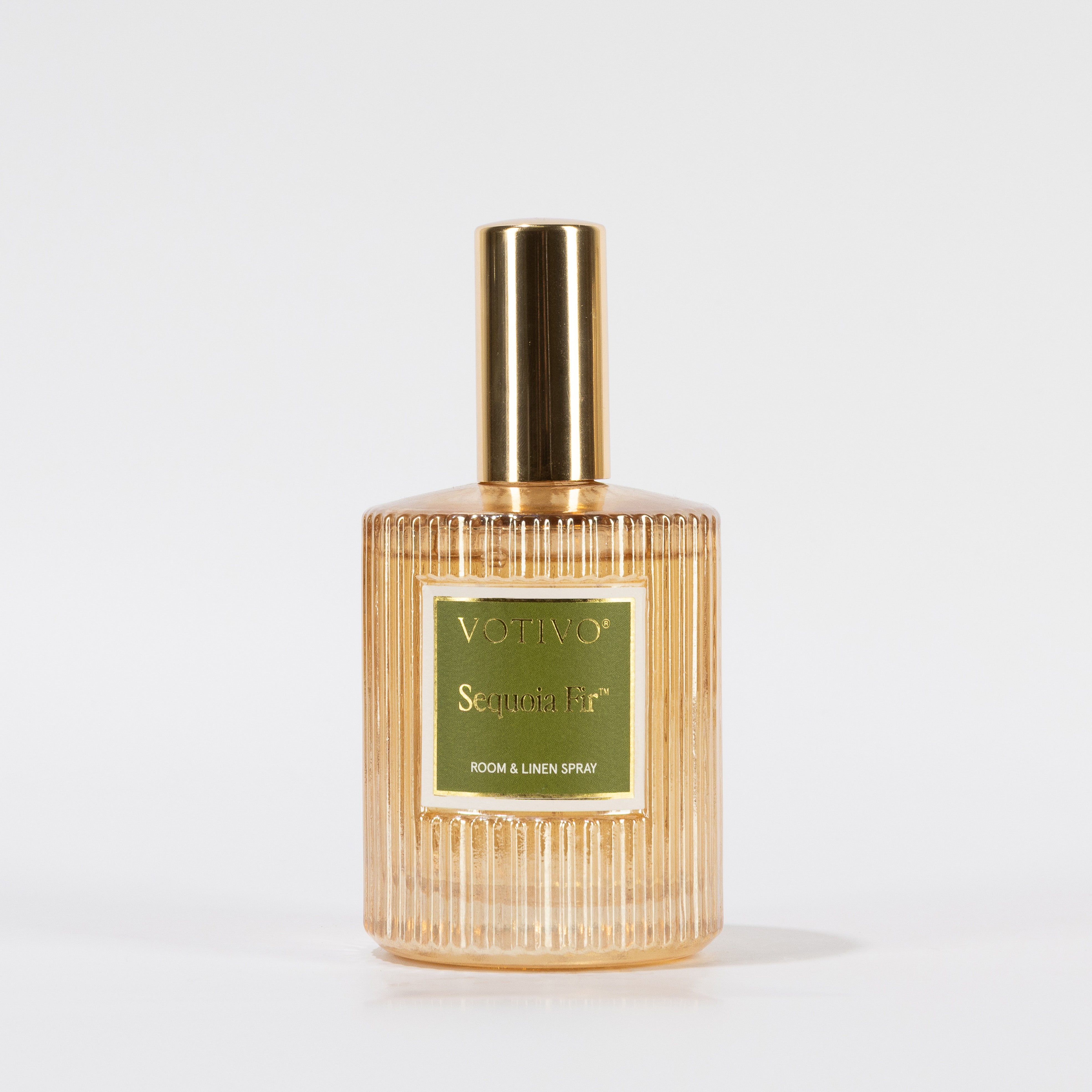 A gold-capped, ribbed glass bottle of Votivo Sequoia Fir Room & Linen Spray with a green and gold label, safe for fabrics, is shown against a plain white background.